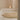Candle on a white surface next to a textured rug in a minimalistic setting.