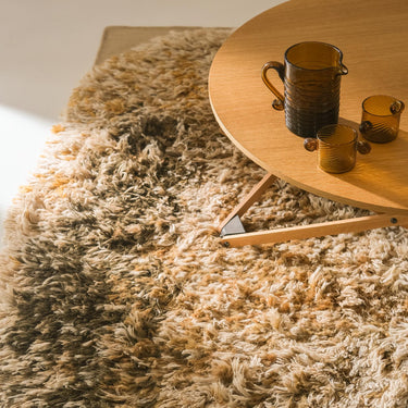 Shaggy beige ochre 70s style rug with a wooden coffee table and glasses on it.