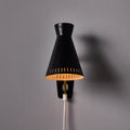 Black wall-mounted midcentury diabolo shaped lamp with plug and brass arm by Mauri Almari on a white background