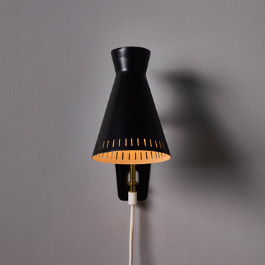 Black wall-mounted midcentury diabolo shaped lamp with plug and brass arm by Mauri Almari on a white background