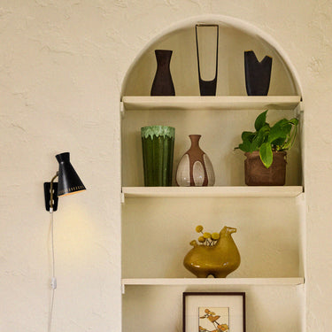 Shelving unit with decorative items and a wall lamp against a white wall.