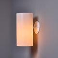 Wall-mounted soft white light fixture with a cylindrical shade on a gray wall