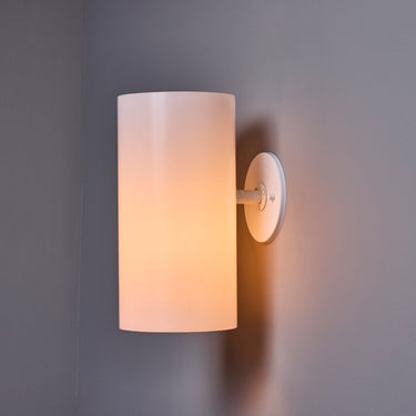 Wall-mounted soft white light fixture with a cylindrical shade on a gray wall