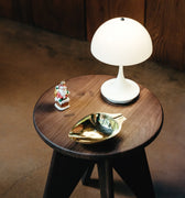 Small wooden table with a white lamp, decorative leaf, and small figurine on a brown floor.