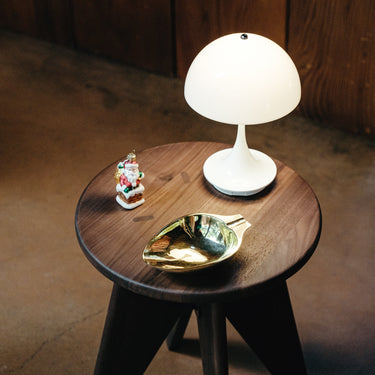 Small wooden table with a white lamp, decorative leaf, and small figurine on a brown floor.