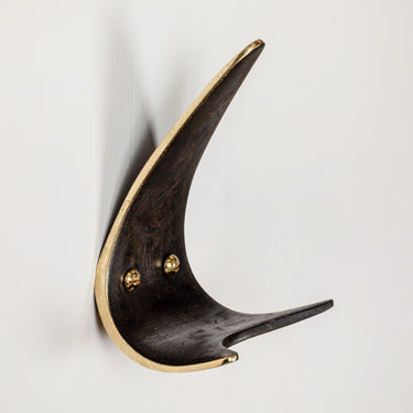 Decorative wall hook with black and gold finish on a light gray background