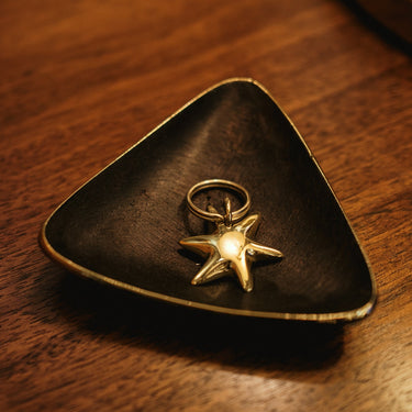 Gold star-shaped ring on a black triangular dish on a wooden surface