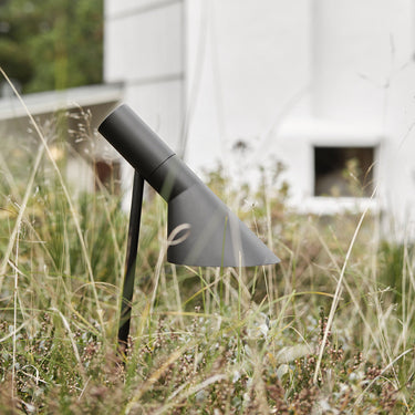 Modern outdoor pathway light in a grassy area with a white building in the background