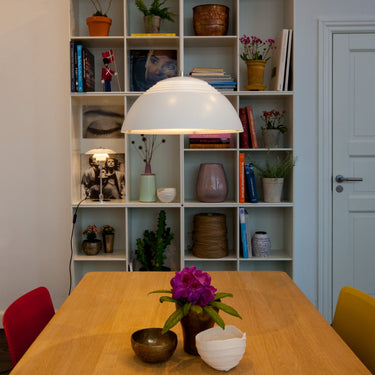 Bookshelf with decorative items a white dome pendant light and a table with a plant in a room.