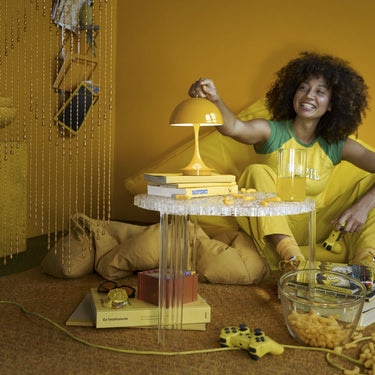 Woman sitting on the floor in a yellow room with a small table and panthella portable lamp.