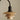 A close-up of a modern pendant light fixture with a curved black metal arm and a tiered shade system in warm beige and cream tones, set against a solid neutral beige background.