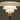 A close-up of a modern table lamp with a tiered, mushroom-shaped frosted glass shade and a matching cylindrical base, shown against a dark warm gray background.