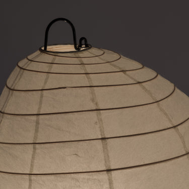 Beige paper lantern with black wire frame on a dark background
