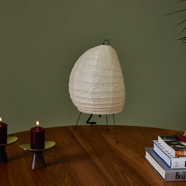 Unlit akari 1N White paper lamp on a wooden table with candles and books against a green wall
