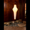 Floor lamp with a textured washi paper shade and black metal base against a wooden wall.