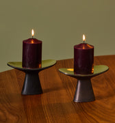 Two purple candles on black holders on a wooden table with a green wall background