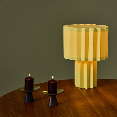 Yellow geometric table lamp on a wooden surface with books and candles