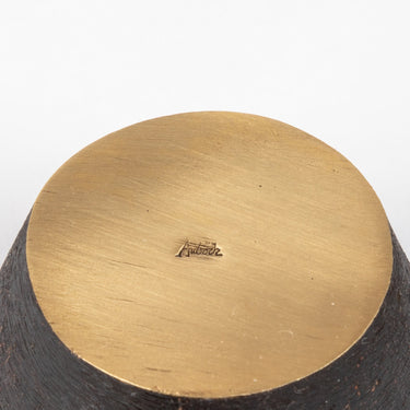 Close-up of a brass crown object with a visible brand logo on a white background