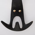 Black brass wall hook with gold screws on a light gray background