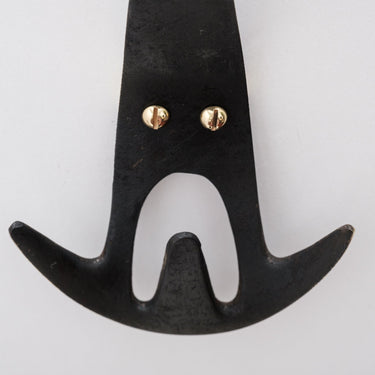 Black brass wall hook with gold screws on a light gray background