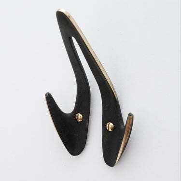 Black brass wall hook with polished brass rim  on a light gray background