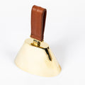 brass cowbell with a brown leather handle on a white background