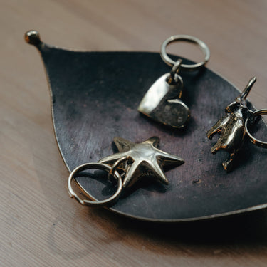 brass heart star and donkey keyrings on a leaf-shaped dish on a wooden surface