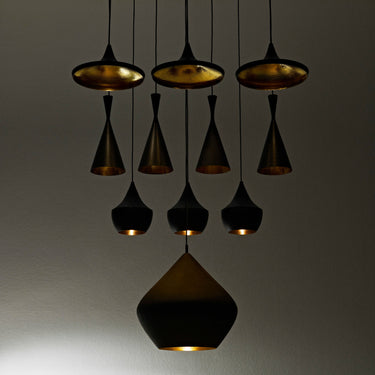 Modern tom dixon pendants on display with gold and black design on a neutral background