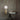 Table lamp with a gold base and white shade on a glass table against a textured wall.