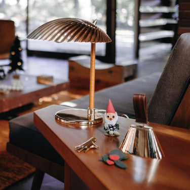 Wooden desk with a lamp, gnome figurine, and decorative bell and tynell lamp in a living room setting.