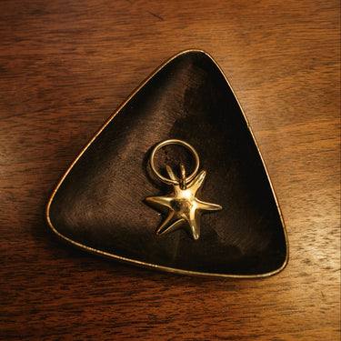 Triangular dark brown dish with a gold star-shaped pendant on a wooden surface