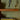 A styled interior scene with wooden floating shelves against an olive-green wall. On the top shelf are two decorative sculptures, one black and one gold.
