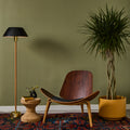 Wooden chair with a floor lamp and plant against a green wall