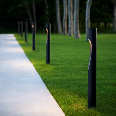 black metal modern outdoor pathway bollard lights along a pathway in a park setting.