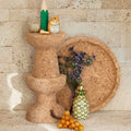 Decorative items including a pineapple, small animal figurine, and fruit on a stone pedestal against a textured wall.