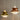 Two modern pendant lights with tiered metallic shades, one in polished gold and the other in copper, hanging against a neutral gray wall.