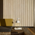 Modern interior with a yellow chair, gray sofa, and  finn juhl white lamp against a wooden paneled wall.