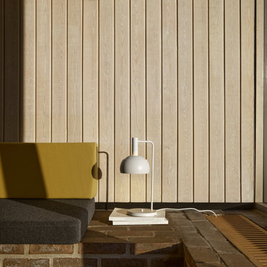 Modern interior with a yellow chair, gray sofa, and  finn juhl white lamp against a wooden paneled wall.