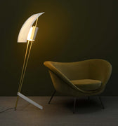 Modern floor lamp with a curved design next to a yellow chair against a dark wall.