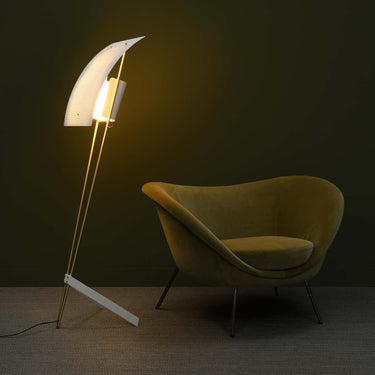 Modern floor lamp with a curved design next to a yellow chair against a dark wall.