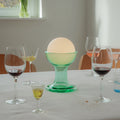Table setting with wine glasses, a vase of tulips, and a green gelato lamp.