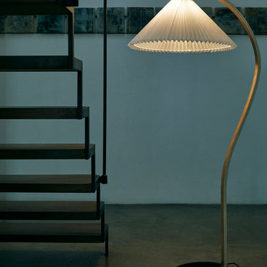 Arc floor lamp with a ribbed shade next to a staircase in a dimly lit room.