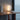 Carlo Nason 'Medusa' table lamp with a frosted white glass shell and warm yellow glow, placed on a wooden desk next to books and glasses in a minimalist room setting.