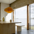 Modern interior with wooden table and bench by large windows overlooking a lake for Two Enlighten