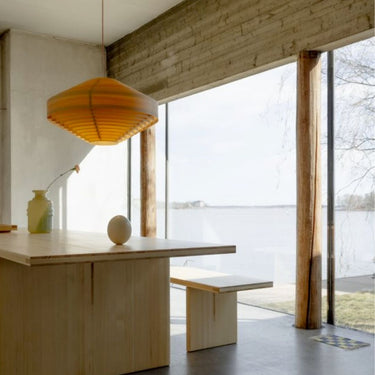 Modern interior with wooden table and bench by large windows overlooking a lake for Two Enlighten