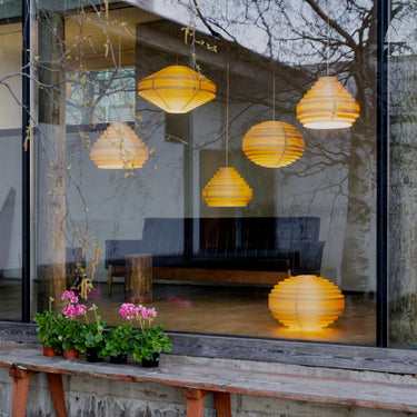 Yellow wood lanterns hanging outside a building with a reflection of a couch Hans-Agne Jakobsson '1003 Hans Pendant' in Pine for Two Enlighten