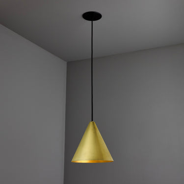 polished brass conical tratten pendant light hanging against a gray wall