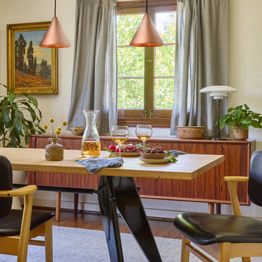 Copper conical pendants over dining room  table with a table set for a meal, featuring wine glasses and a bottle.