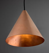 copper conical pendant in unpolished raw metal against a grey background with black cord