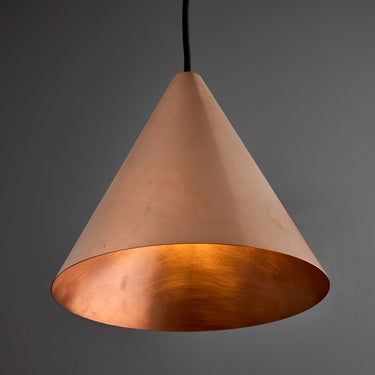 copper conical pendant in unpolished raw metal against a grey background with black cord